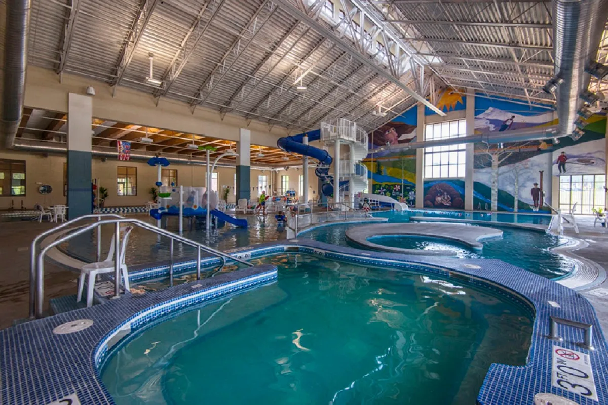A lively indoor recreation center featuring water slides, swimming pools, children playing, and colorful murals. The environment is dynamic and family-friendly, emphasizing fun and relaxation.