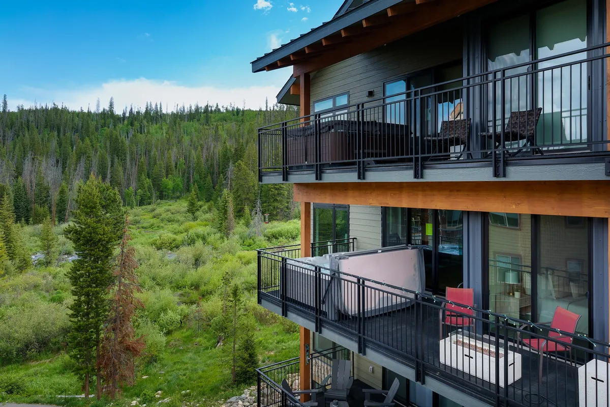 This exterior shot features the condo's balconies overlooking a lush, green landscape, with a hot tub in the foreground. The scene is tranquil, suggesting relaxation and scenic enjoyment. The image hints at social spaces like balconies for gathering and an inviting hot tub for unwinding, all set during the golden hour.
