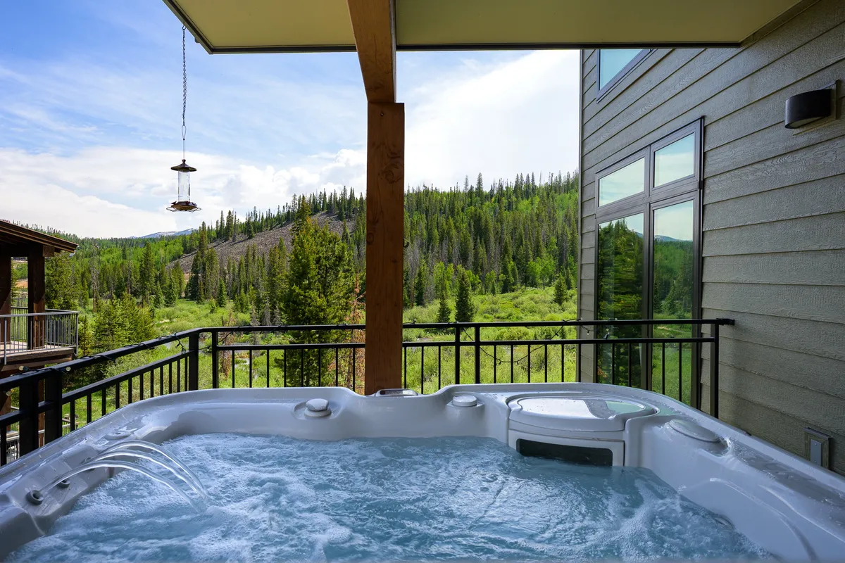 An outdoor hot tub set on a deck with mountain views and lush greenery. The setting is tranquil, suggesting relaxation and luxury, and offers views perfect for unwinding after a day of adventure.