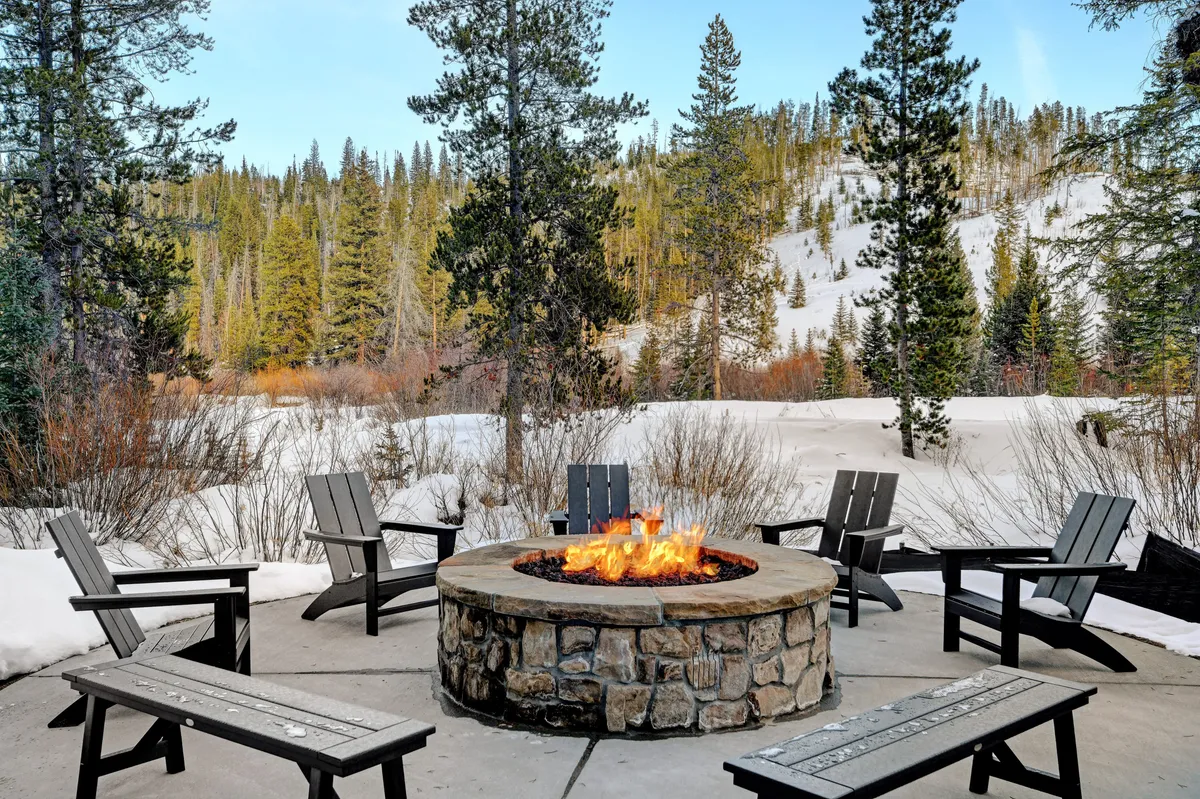A cozy fire pit area surrounded by seating, set against a snow-covered ground and a forest backdrop. The scene evokes warmth, camaraderie, and memorable evenings shared with other guests.