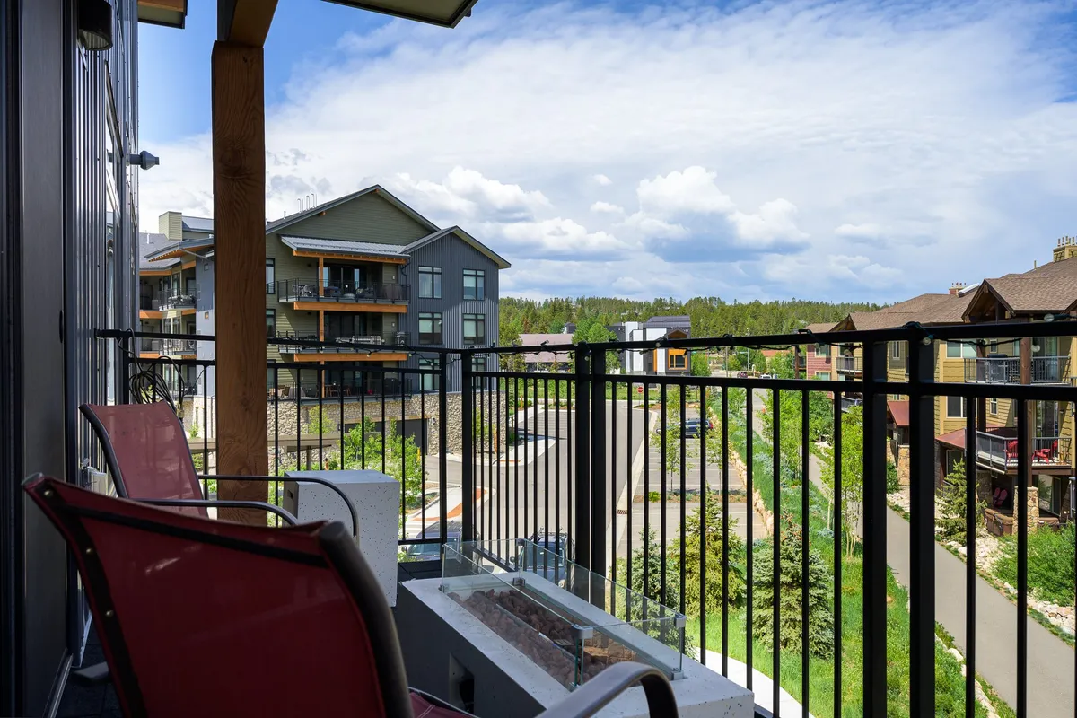 A serene balcony scene with comfortable chairs positioned to overlook a sweeping landscape view. The architecture of the building is visible, blending harmoniously with its alpine surroundings. The image exudes tranquility, suggesting moments of relaxation, morning coffee, or evening socializing.