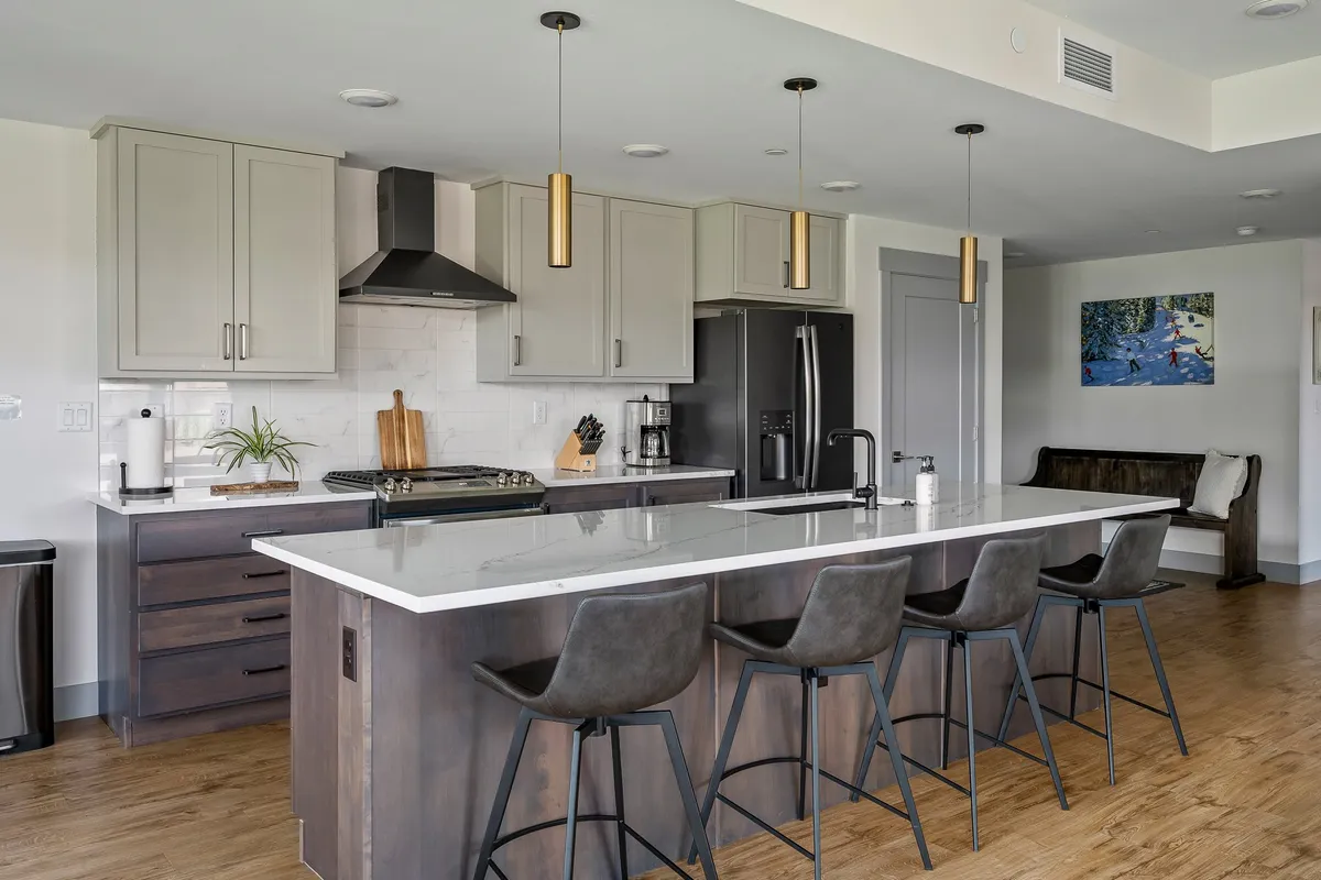 A contemporary kitchen with a spacious granite island, stainless steel appliances, pendant lighting, and bar stools. The layout encourages interaction, with ample space for cooking, entertaining, and casual meals.