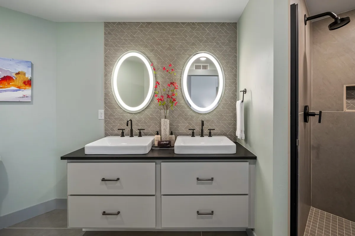 A modern, spa-inspired bathroom with double sink vanity, oval mirrors, a decorative plant, and subtle artwork. The clean lines and calming decor evoke the feel of a high-end hotel spa, ideal for self-care and rejuvenation.