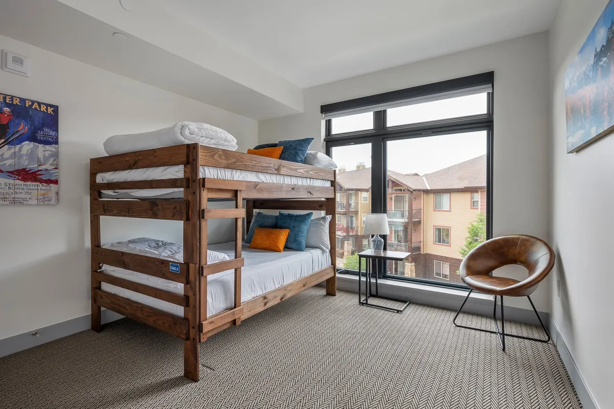A playful bunk room featuring a sturdy full-over-full bunk bed with accent pillows, a large window letting in natural light, and a cozy chair in the corner. The room feels inviting for kids or friends, encouraging late-night chats and fun sleepovers.